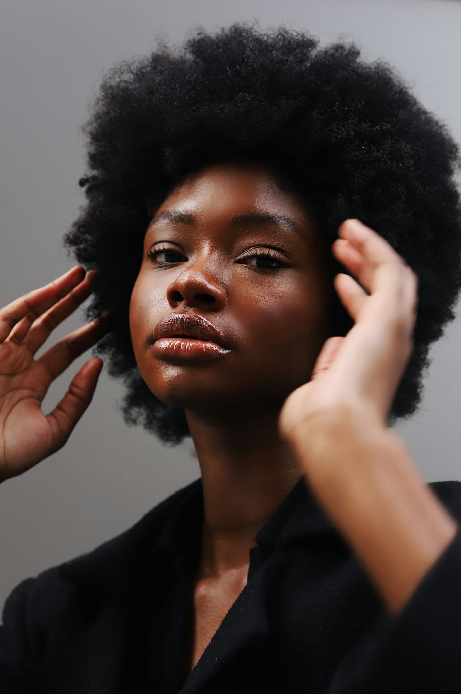 Woman with a voluminous afro and glossy lips framing her face with both hands