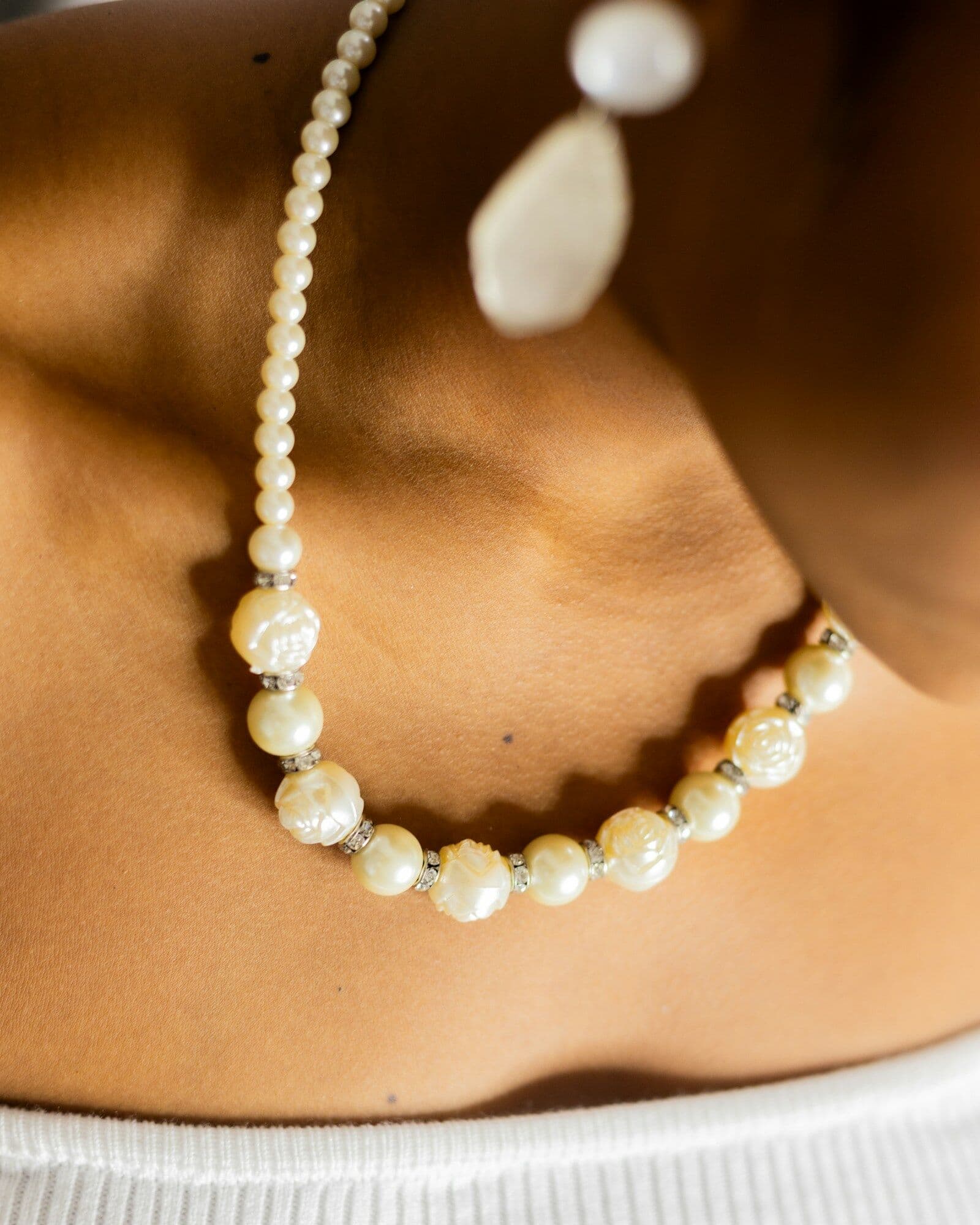 Close-up of a pearl necklace and earring resting against smooth, deep brown skin