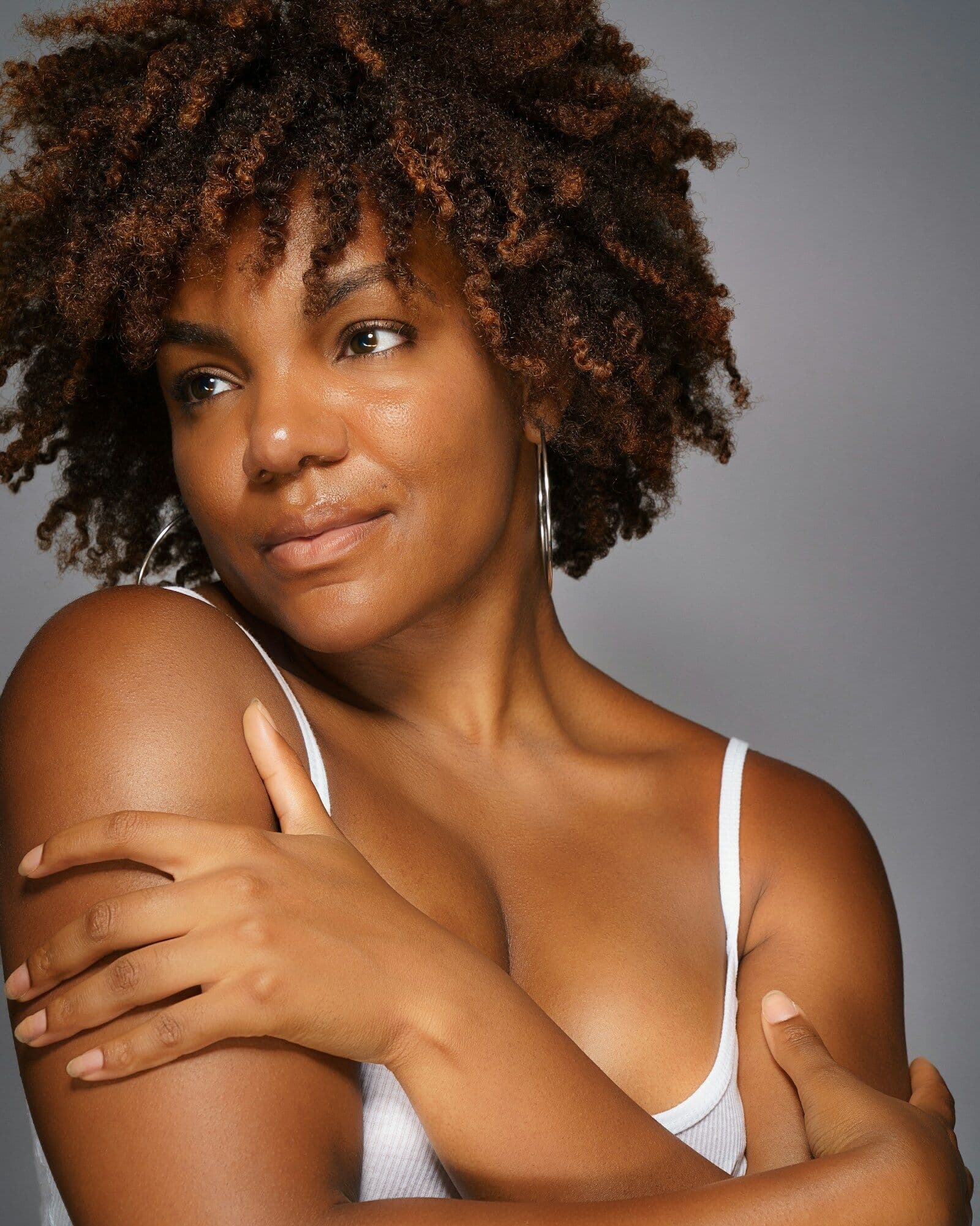 Smiling woman with natural curls embracing her shoulders, relaxed and confident in her skin