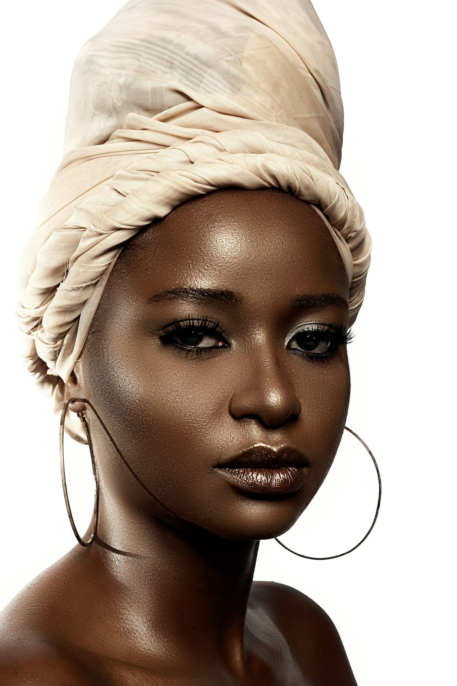 Portrait of a woman in an ivory head wrap and gold hoop earrings with luminous skin