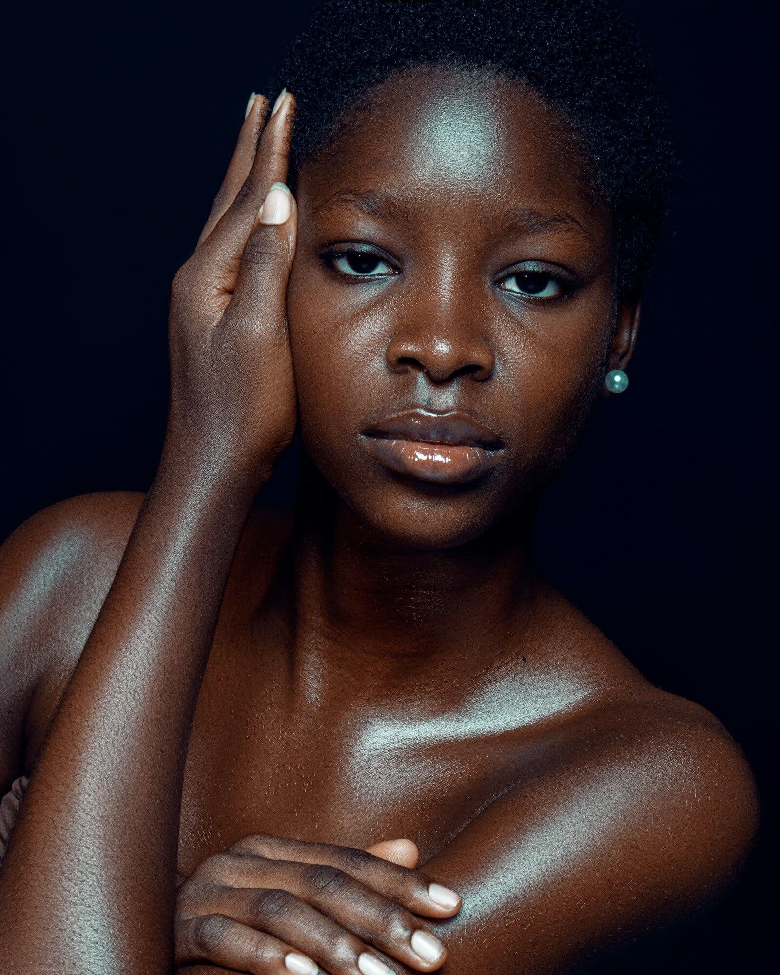 Studio beauty portrait of a woman with deep brown skin and short hair, one hand resting at her temple