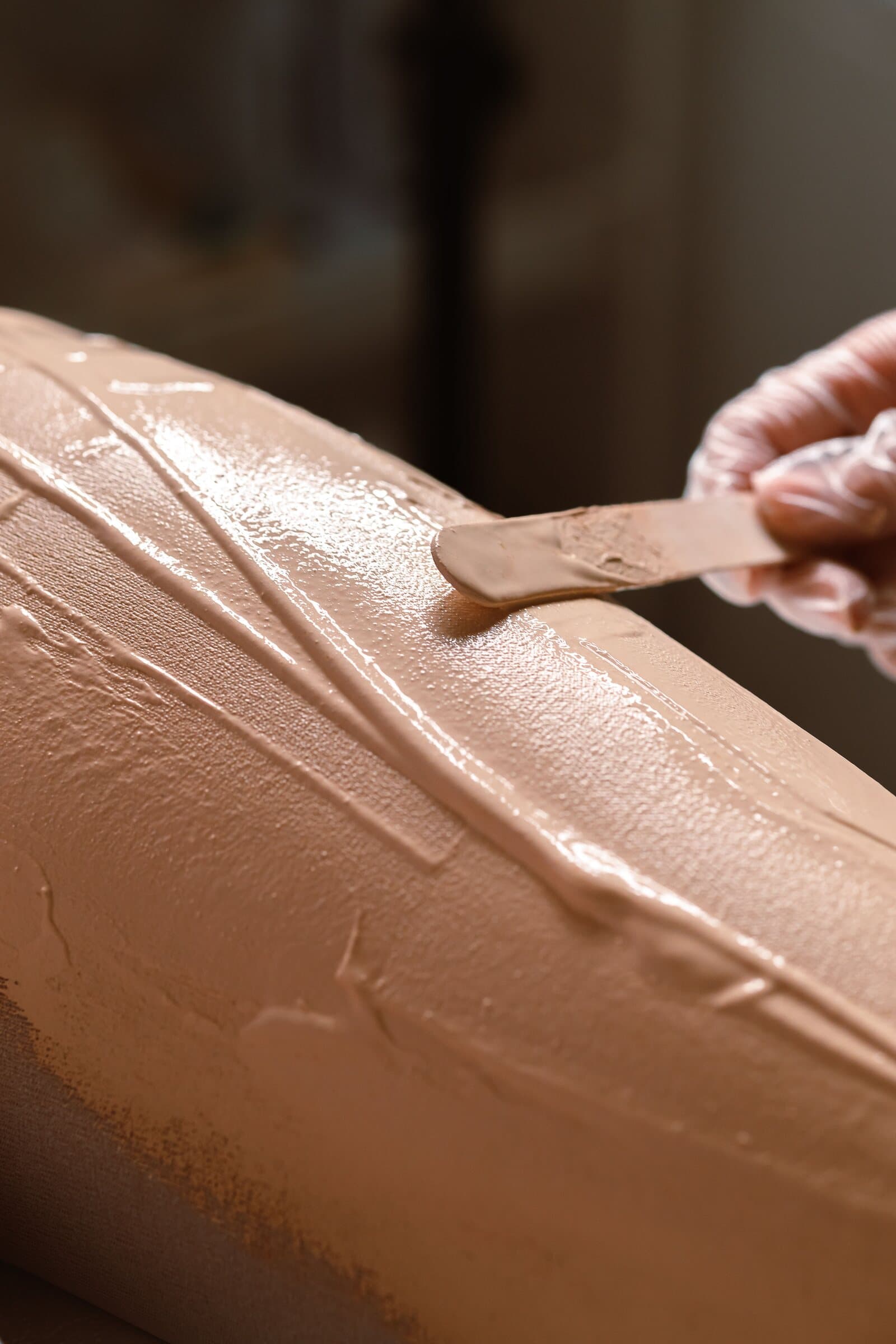 Close-up of warm wax being smoothed along a leg with a wooden spatula